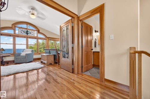 Hardwood flooring throughout, arched window with stained glass accent, paneled interior doors, wood-finish trim, and a ceiling fan with integrated lighting - 51 Itaska Beach, Rural Leduc County, AB 