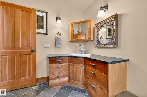 Hardwood door with black hardware, corner vanity with dark countertops, under-mount sink, and built-in wood cabinetry, complemented by square floor tiles - 51 Itaska Beach, Rural Leduc County, AB 