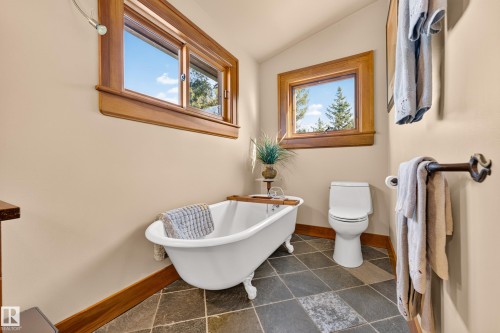 Freestanding clawfoot tub, natural wood window trim, dark slate-style floor tiling, and a white toilet - 51 Itaska Beach, Rural Leduc County, AB 