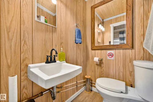 Wood-finish wall paneling, wall-mounted sink with a dark bronze faucet, framed mirror, and a white toilet - 51 Itaska Beach, Rural Leduc County, AB 