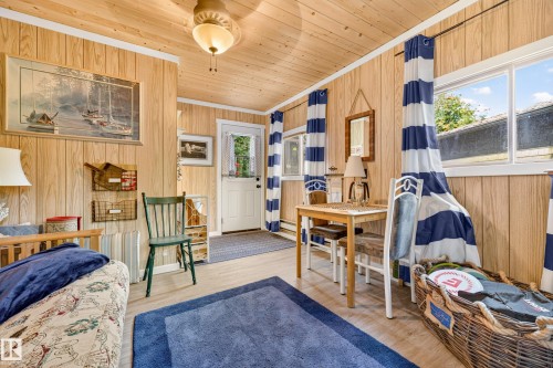 Wood-finish paneling, wood-finish flooring, white ceiling fan, multiple windows, and a built-in wall heater - 51 Itaska Beach, Rural Leduc County, AB 