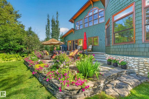 Extensive stone patio with built-in planter beds, natural stone retaining walls, and a manicured lawn - 51 Itaska Beach, Rural Leduc County, AB 