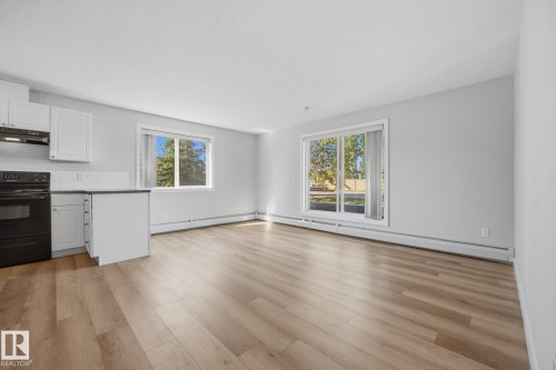 Open-concept living area featuring wood-finish flooring, white cabinetry, black appliances, and large windows - #122 240 Spruce Ridge Rd, Spruce Grove, AB 
