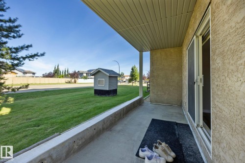 Covered concrete patio with sliding glass door access, stucco exterior, and a manicured lawn - #122 240 Spruce Ridge Rd, Spruce Grove, AB 