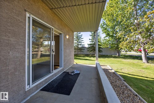 Covered patio with textured stucco exterior, sliding glass door, and integrated wall sconce lighting - #122 240 Spruce Ridge Rd, Spruce Grove, AB 