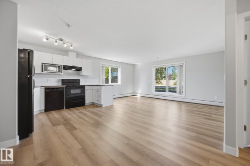 Open-concept living space with wood-finish flooring, white cabinetry, track lighting, and a kitchen island - #122 240 Spruce Ridge Rd, Spruce Grove, AB 