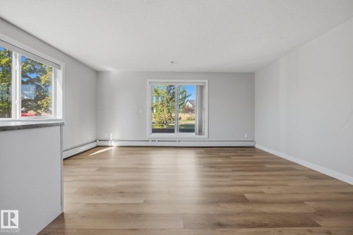 Wood-finish flooring, light gray wall paint, white trim, sliding glass door, and large window - #122 240 Spruce Ridge Rd, Spruce Grove, AB 