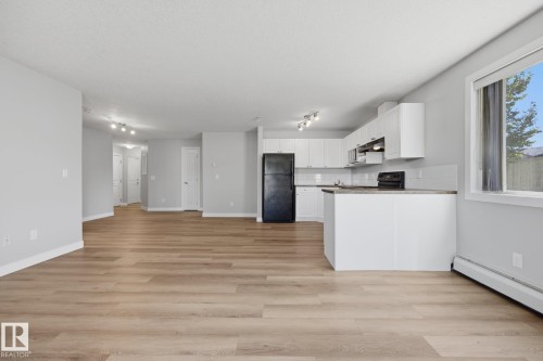 Open-concept living area featuring wood-finish flooring, white cabinetry, track lighting, and a kitchen island with a countertop - #122 240 Spruce Ridge Rd, Spruce Grove, AB 