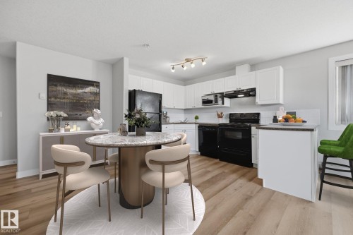 Open-concept kitchen featuring wood-finish flooring, white cabinetry, black appliances, track lighting, and a breakfast bar - #122 240 Spruce Ridge Rd, Spruce Grove, AB 