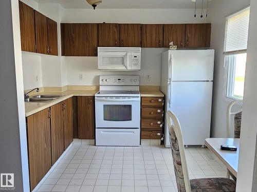 Kitchen featuring wood-finish cabinetry, laminate countertops, a double basin stainless steel sink, tile flooring, and a window with blinds - 14674 54 Street Northwest, Edmonton, AB 