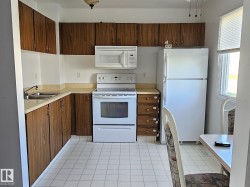 Kitchen featuring wood-finish cabinetry, laminate countertops, a double basin stainless steel sink, tile flooring, and a window with blinds - 