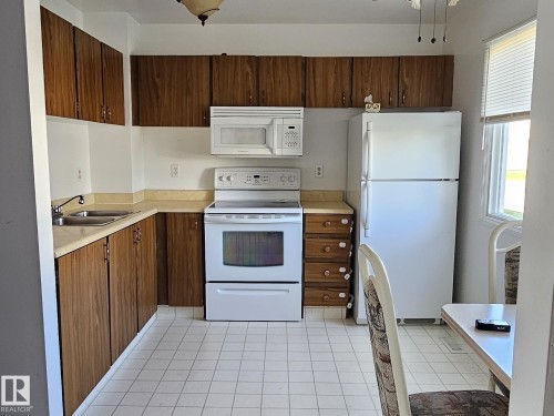 Kitchen featuring wood-finish cabinetry, white appliances, dual basin sink, and tile flooring - 14674 54 Street Northwest, Edmonton, AB 