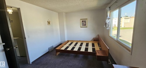 Carpeted room with white walls, a large window, and a wood-finish door frame - 14674 54 Street Northwest, Edmonton, AB 