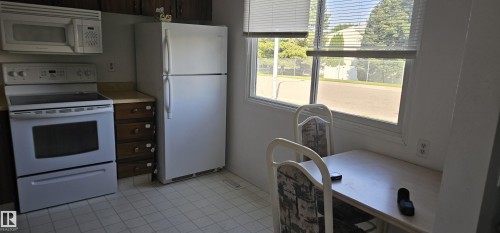 Kitchen featuring wood cabinetry, white appliances, and a window with blinds - 14674 54 Street Northwest, Edmonton, AB 