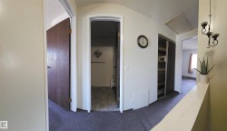 Carpeted hallway featuring multiple doorways, a built-in closet with shelving, and an overhead access panel - 