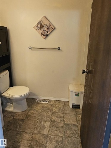 White toilet with an adjacent dark-wood finish storage cabinet, a chrome towel bar, and square tile flooring - 14674 54 Street Northwest, Edmonton, AB 