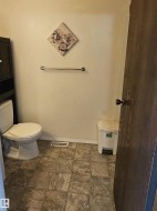 White toilet with an adjacent dark-wood finish storage cabinet, a chrome towel bar, and square tile flooring - 