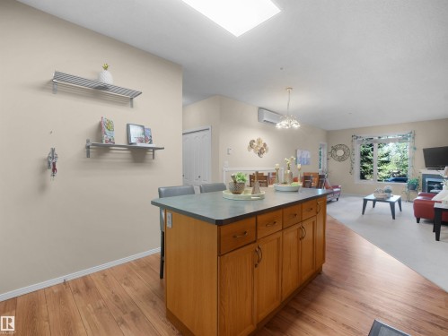 Kitchen island with integrated cabinetry and seating area, wood-finish flooring, and a large skylight - #206 12111 51 Av Nw, Edmonton, AB 