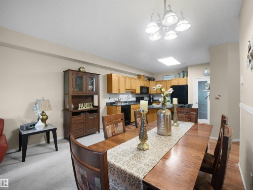 Open-concept dining area featuring a multi-light chandelier, skylight, wood-finish flooring, and direct access to the kitchen with wood cabinetry - #206 12111 51 Av Nw, Edmonton, AB 