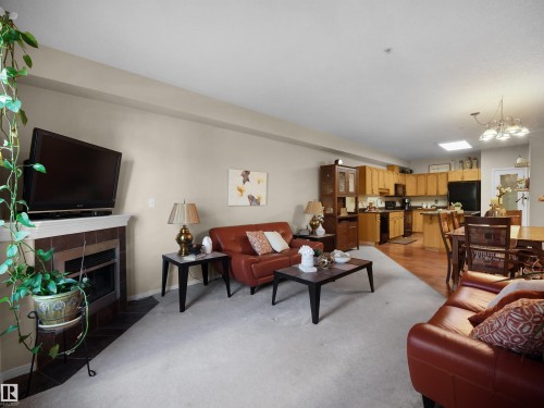 Open concept living space featuring a fireplace with a tiled surround, a kitchen with wood cabinetry, and a dining area with a chandelier - #206 12111 51 Av Nw, Edmonton, AB 