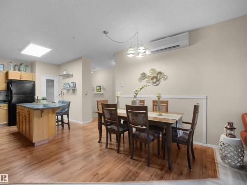 Wood-finish flooring throughout, kitchen island with counter seating, shaker-style cabinetry, recessed ceiling lighting, and wall-mounted air conditioning unit - #206 12111 51 Av Nw, Edmonton, AB 