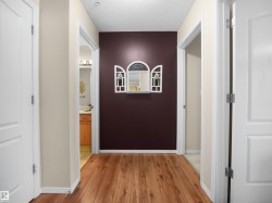 Hallway featuring warm wood-finish flooring, soft neutral wall finishes, and multiple white panel doors - 