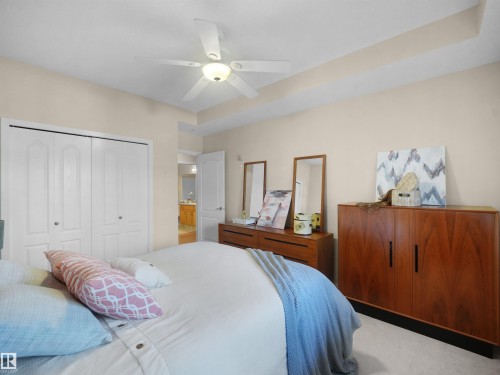 Recessed tray ceiling with a ceiling fan, bi-fold closet doors, and light-colored carpeting - #206 12111 51 Av Nw, Edmonton, AB 