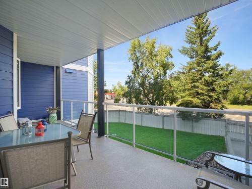 Covered outdoor balcony featuring a speckled concrete surface, glass and metal railing, and blue exterior siding - #206 12111 51 Av Nw, Edmonton, AB 