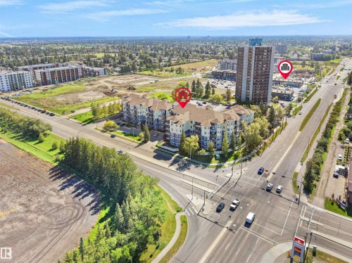 Multi-story residential buildings with balconies, adjacent to a wide paved road, and surrounded by mature trees - #206 12111 51 Av Nw, Edmonton, AB 