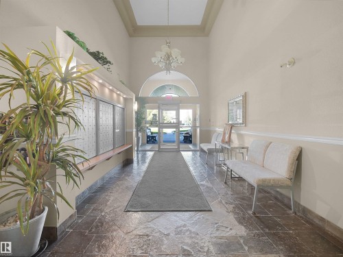Entryway featuring a vaulted ceiling with a chandelier, slate flooring, and a glass-paneled door with an arched transom - #206 12111 51 Av Nw, Edmonton, AB 