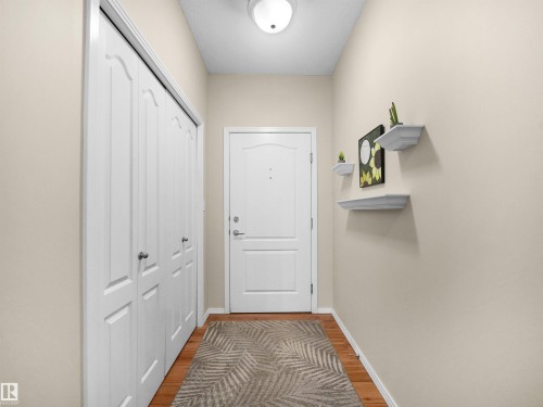Entryway featuring wood-finish flooring, a flush-mount ceiling light, paneled bi-fold closet doors, a paneled entry door, and decorative wall shelving - #206 12111 51 Av Nw, Edmonton, AB 