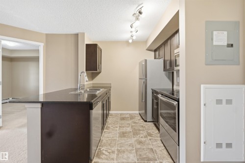Kitchen featuring dark cabinetry, stainless steel appliances, track lighting, and a double basin sink - #225 1510 Watt Dr Sw, Edmonton, AB 