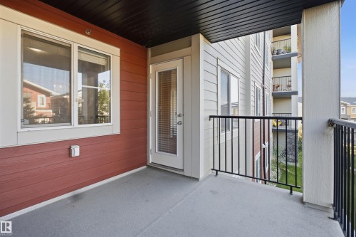 Covered outdoor patio with a concrete surface, white trim windows, a glass-paneled door, and black metal railings - #225 1510 Watt Dr Sw, Edmonton, AB 