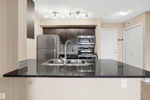 Kitchen featuring a double basin stainless steel sink, dark cabinetry, and stainless steel appliances - #225 1510 Watt Dr Sw, Edmonton, AB 