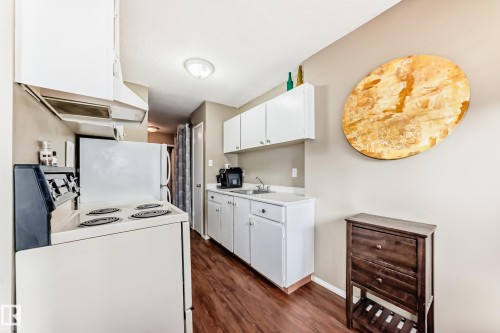 Kitchen featuring wood-finish flooring, white cabinetry, and a range with overhead ventilation - #302 10606 123 St Nw, Edmonton, AB 
