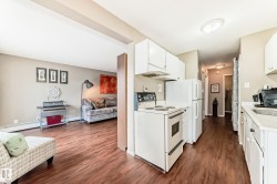 Kitchen featuring white cabinetry and appliances, alongside wood-finish flooring extending into the adjoining room - 