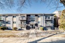 Multi-story building with textured gray and beige facade, dark stone accent wall, multiple private balconies with dark railings, and a central entrance with large windows - #302 10606 123 St Nw, Edmonton, AB 