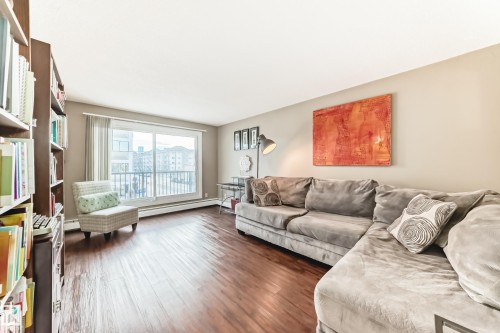Spacious living area featuring wood-finish flooring, a full-height built-in bookcase, and a large sliding glass door with a balcony access - #302 10606 123 St Nw, Edmonton, AB 
