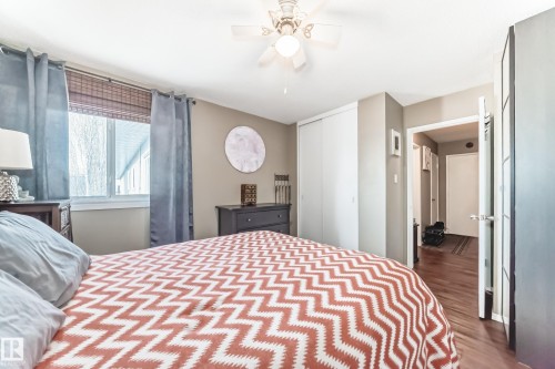 Bedroom featuring a ceiling fan with integrated lighting, wood-finish flooring, a window with blinds, and sliding closet doors - #302 10606 123 St Nw, Edmonton, AB 