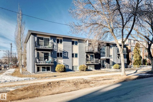 Multi-story building featuring a gray brick exterior, multiple balconies with black railings, and a sidewalk along the property - #302 10606 123 St Nw, Edmonton, AB 