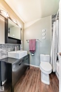Modern bathroom featuring a rectangular vessel sink, dark wood-finish vanity, wood-finish flooring, and a tiled shower surround - 