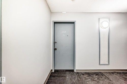 Wall-mounted sconce with circular light fixture, gray painted door with metal hardware, and patterned floor covering - #302 10606 123 St Nw, Edmonton, AB 