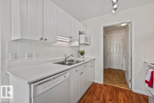 Kitchen featuring wood-finish flooring, white cabinetry with silver-tone hardware, a stainless steel double basin sink, and a built-in microwave - #92 13320 124 St Nw, Edmonton, AB 