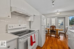 Kitchen featuring white cabinetry, a tile backsplash, a built-in range with an overhead hood, and a refrigerator - 