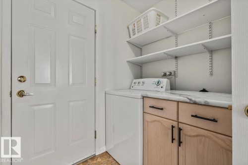 White paneled door with brass hardware, adjustable wall-mounted shelving, wood-finish cabinetry, and a stone-finish countertop - #92 13320 124 St Nw, Edmonton, AB 