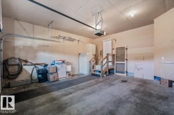 Attached garage with a concrete floor, automatic garage door opener, and interior access via a wooden staircase - 