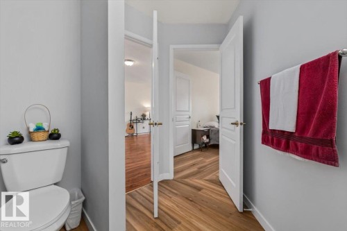 White toilet with a dual-flush mechanism, light gray wall paint, white trim, and wood-finish flooring - #92 13320 124 St Nw, Edmonton, AB 