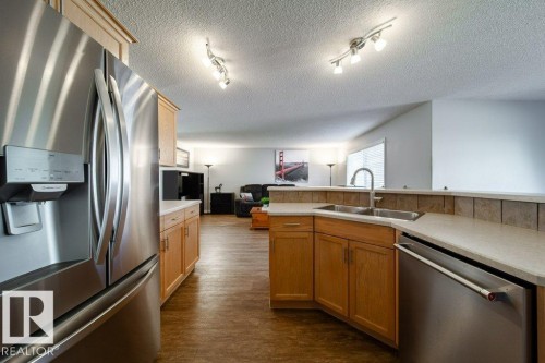 Kitchen featuring stainless steel appliances, wood-finish cabinetry, tile backsplash, and track lighting - 16120 138 Street Nw, Edmonton, AB 