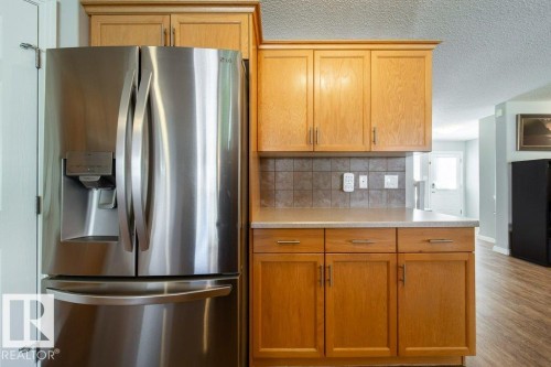 Stainless steel refrigerator, wood-finish cabinetry, tile backsplash, and light-toned countertops - 16120 138 Street Nw, Edmonton, AB 
