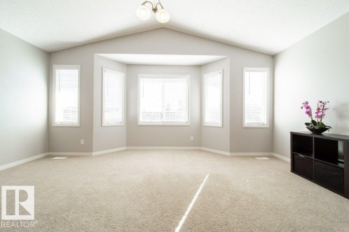 Spacious room featuring vaulted ceilings, recessed bay windows, neutral carpet flooring, and a semi-flush mount light fixture - 16120 138 Street Nw, Edmonton, AB 